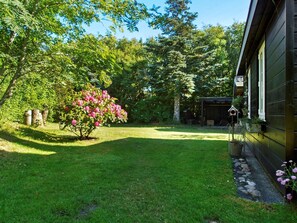 A well-maintained garden with a lawn, a flowering bush, and a wooden structure in the background.