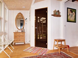 A room with a wooden dresser, a mirror, a door leading to a balcony, a small wooden stool, and a colorful rug.