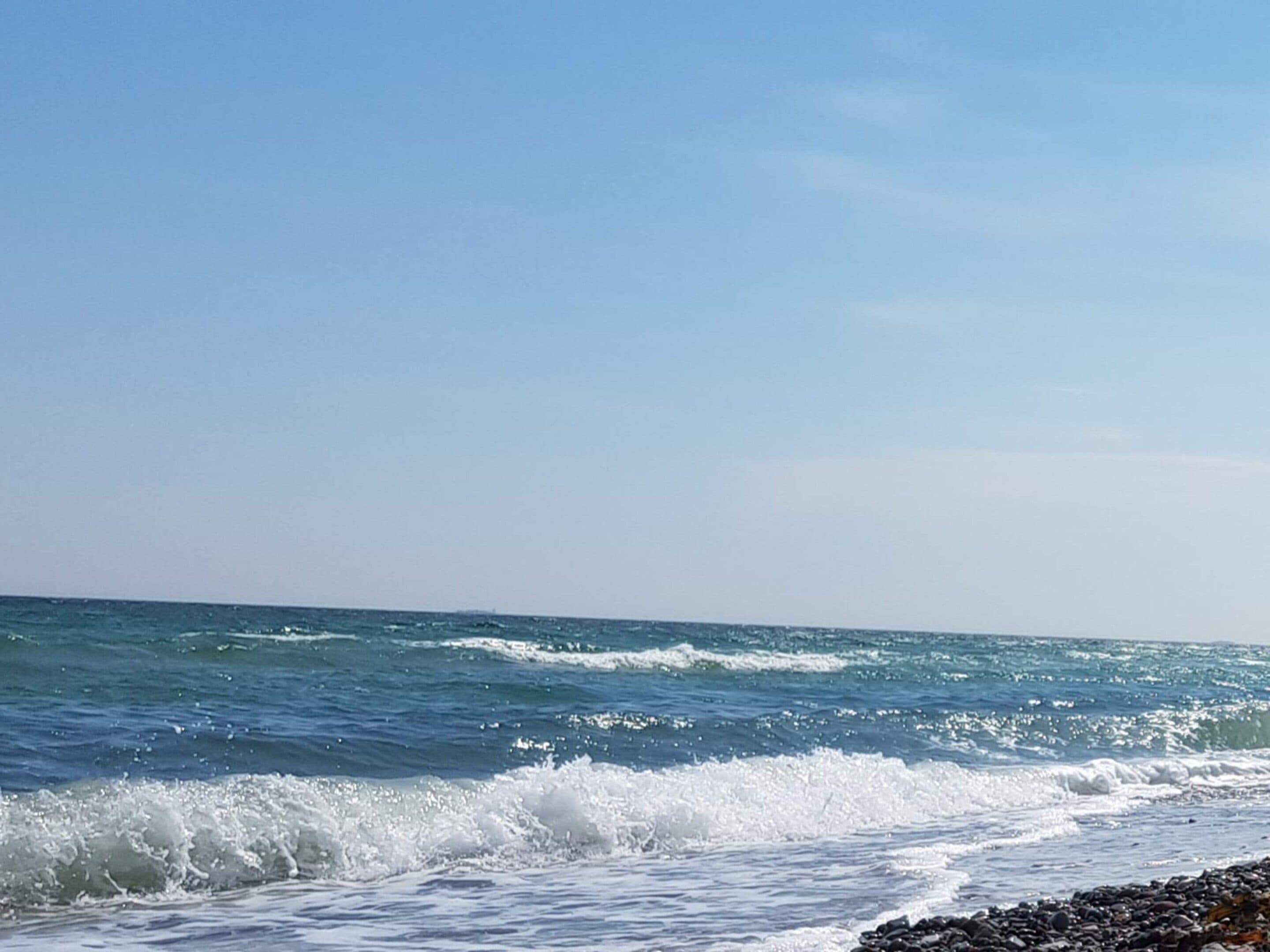 Una playa con olas rompiendo sobre una costa rocosa bajo un cielo despejado.