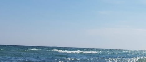 Una playa con olas rompiendo sobre una costa rocosa bajo un cielo despejado.