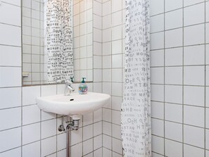 Une salle de bain avec un lavabo blanc, un miroir et un rideau de douche orné de motifs ou d’inscriptions.