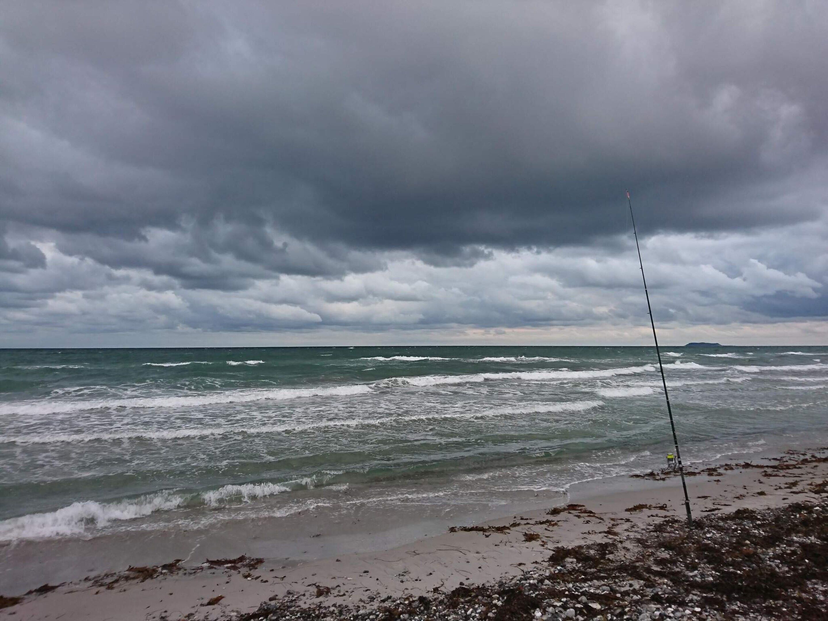 A beach with waves, a fishing rod, and a cloudy sky.