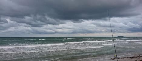 A beach with waves, a fishing rod, and a cloudy sky.