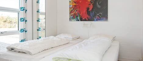 A room with two beds, a window with curtains, and a painting on the wall.