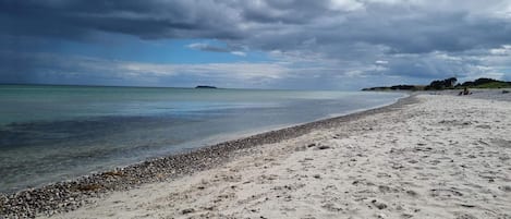Una playa con costa pedregosa, aguas tranquilas y cielo nublado.