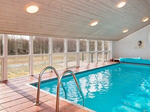 An indoor swimming pool with a clear view of the outdoors through large windows, a tiled floor, and a wooden ceiling. - 4 Star Holiday Home in Ebeltoft (Ebeltoft)