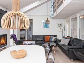 Un salon moderne avec une cheminée, un canapé en cuir noir et un coin repas doté d’une table blanche.
