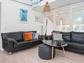 A modern living room with a black leather sofa, a round coffee table, and a grey ottoman. There are two framed artworks on the wall, a floor lamp, and a hanging pendant light. - 4 Star Holiday Home in Ebeltoft (Ebeltoft)