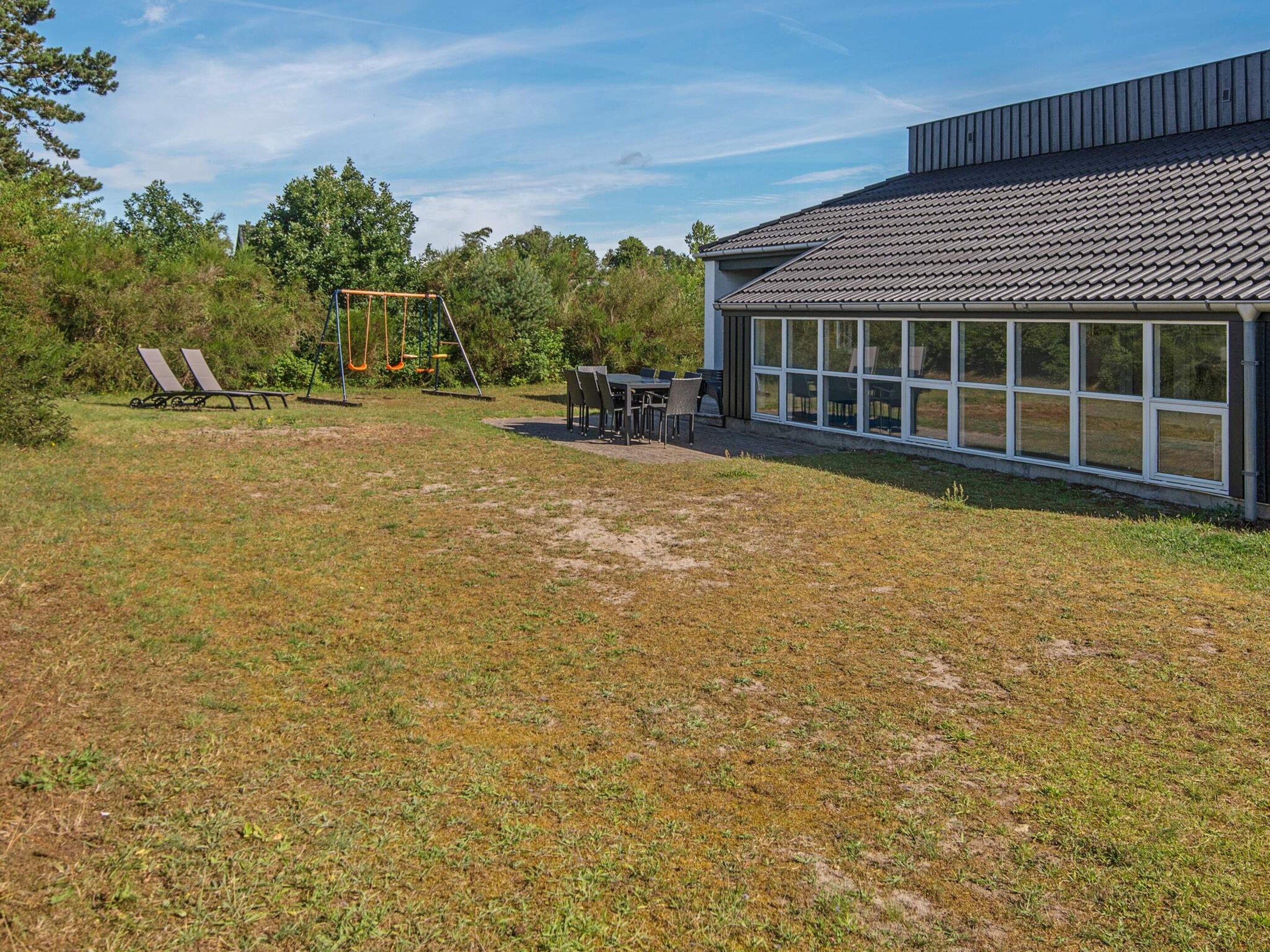 A backyard with a swing set, a dining area with chairs and a table, and a building with large windows.