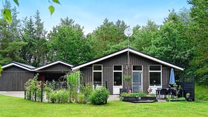 A two-story building with a sloped roof, a fenced yard, and a small garden area with plants and a flower pot. - 4 Star Holiday Home in Saeby (Sæby)