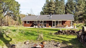 Une cabane en rondins moderne, dotée d’un toit en tuiles, d’un porche couvert et d’un foyer extérieur dans le jardin.