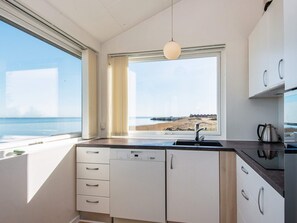 A modern kitchen with a view of the sea, a dishwasher, and a kettle.