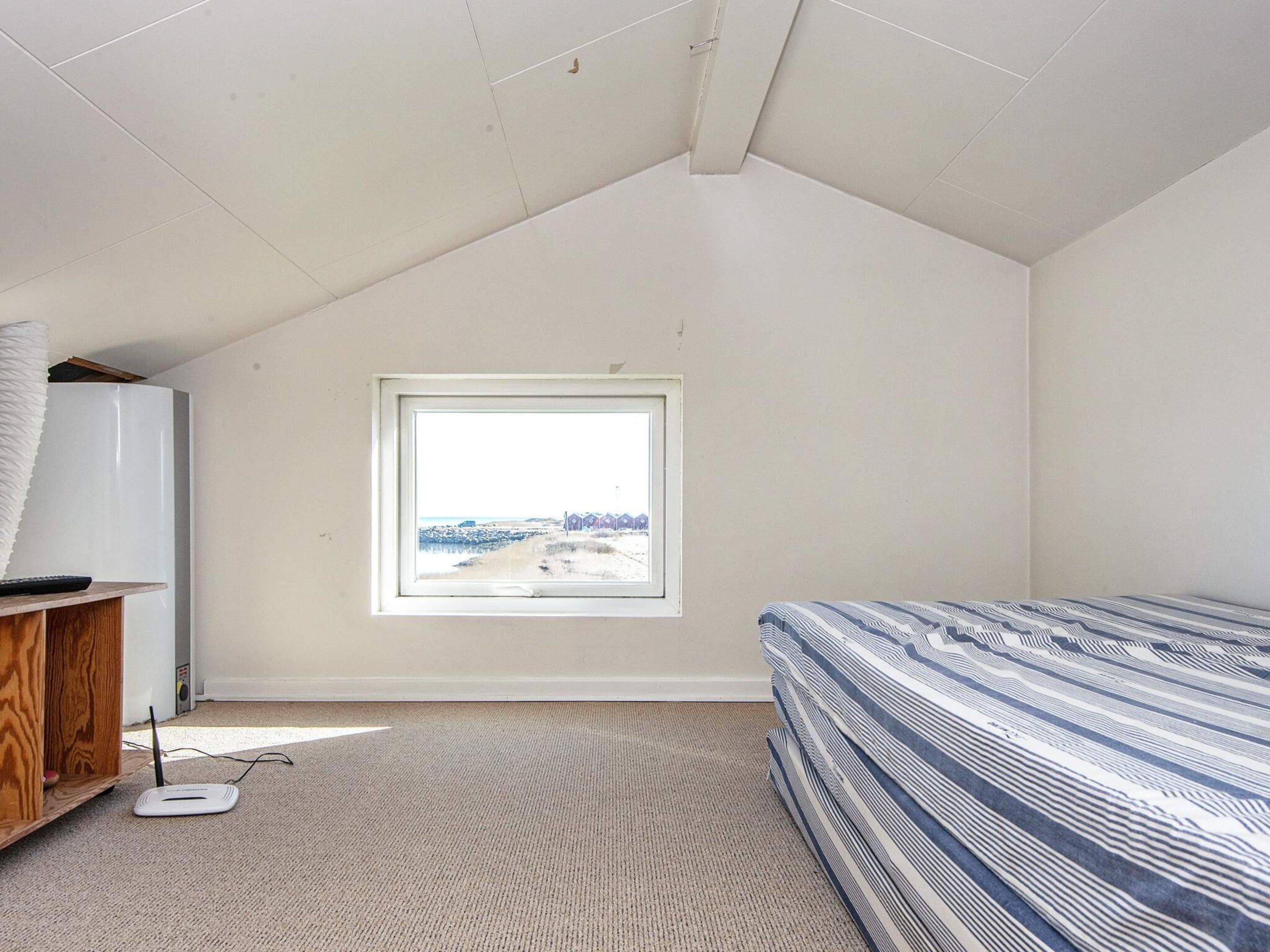A bedroom with a sloped ceiling, a window with a view, a bed with patterned bedding, and a desk with a lamp.