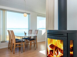 A room with a table and chairs, a fireplace, and a view of the sea through large windows.
