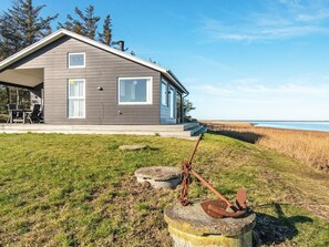 A modern house with a covered patio, a grassy yard, and a view of the water.