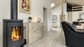 A modern living room with a wood-burning stove, a dining area, and a kitchen. - Roomy Holiday Home in Falster near Sea (Vaeggerlose)