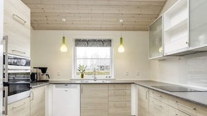 A modern kitchen with light wood cabinets, a white dishwasher, and a window with a view of the outside. - Roomy Holiday Home in Falster near Sea (Vaeggerlose)