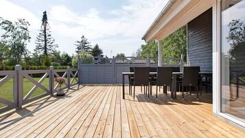 A wooden deck with outdoor furniture, a gated entrance, and a view of trees and sky.