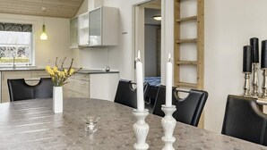 A dining area with a round table, chairs, a vase with flowers, candles, and a clock on the wall. - Roomy Holiday Home in Falster near Sea (Vaeggerlose)
