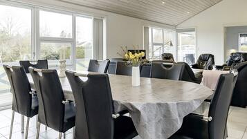 A modern dining room with a large table, black chairs, and a vase of yellow flowers.