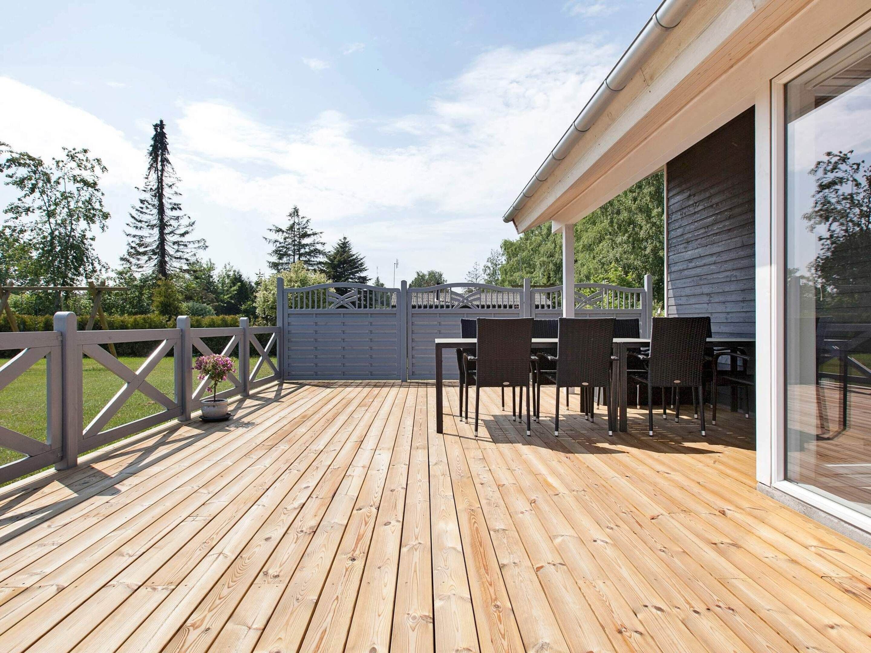 A wooden deck with outdoor furniture, a gated entrance, and a building with large windows.