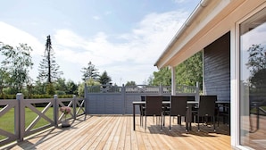 A wooden deck with outdoor furniture, a gated entrance, and a building with large windows. - Roomy Holiday Home in Falster near Sea (Vaeggerlose)
