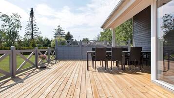 A wooden deck with outdoor furniture, a gated entrance, and a building with large windows.