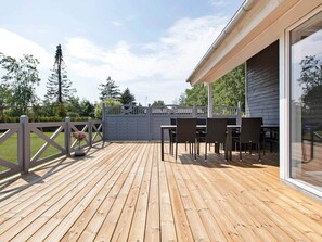 Une terrasse en bois avec des meubles d’extérieur, une entrée fermée par un portail et un bâtiment doté de grandes fenêtres.