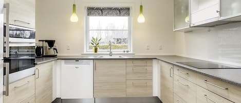 A modern kitchen with light wood cabinets, a built-in dishwasher, and a window with a view.