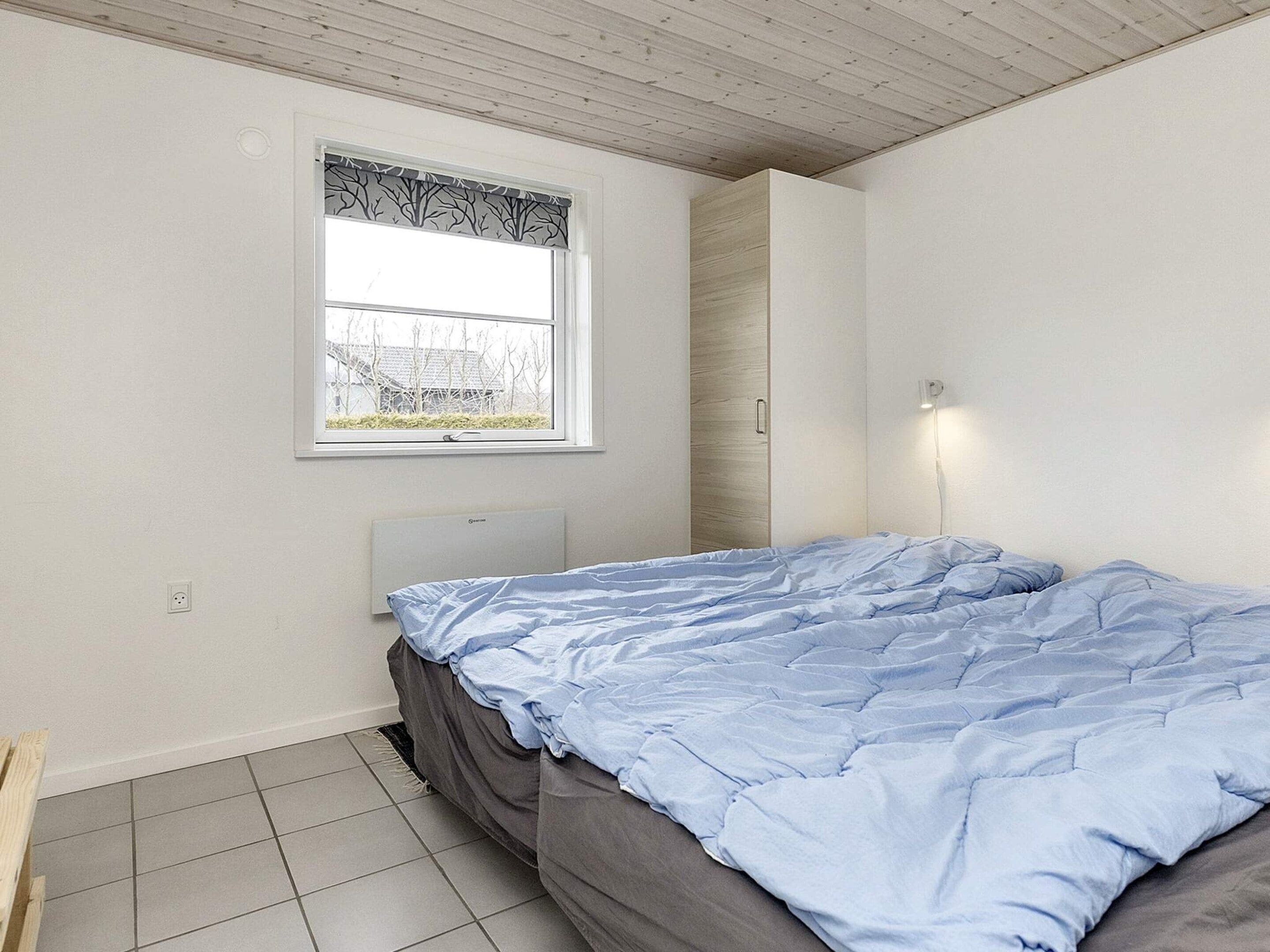 Un dormitorio con cama, ventana con cortina, luz empotrada en la pared y radiador.