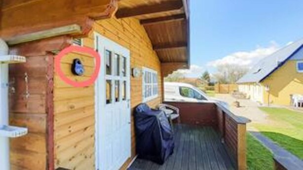 A wooden cabin with a porch, a door with a red circular decoration, and a covered outdoor seating area. - Spacious Holiday Home in Vinderup near Fjord (Vinderup)