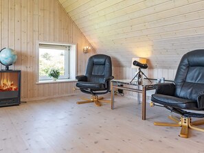 Une pièce chaleureuse avec deux fauteuils en cuir, un plafond en bois, une cheminée, un globe terrestre et une fenêtre donnant sur un beau paysage.