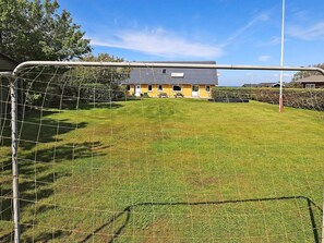 Un espace extérieur clos, avec un terrain herbeux, un bâtiment jaune doté d’un toit gris et un ciel dégagé.