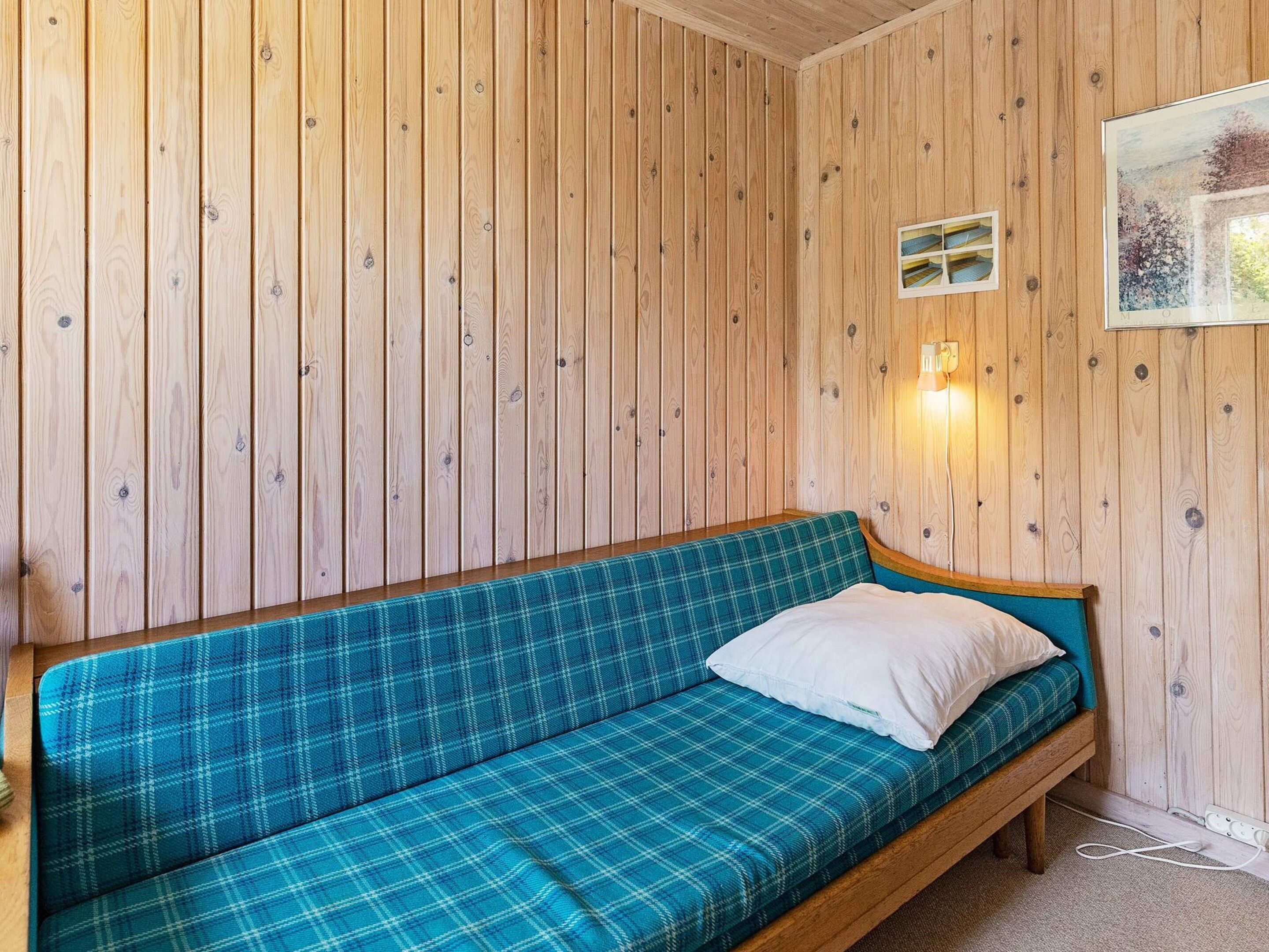 A wooden-paneled room with a blue plaid sofa and a white pillow.