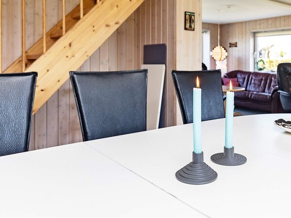 Uma mesa de jantar com duas velas, uma escada de madeira e um sofá de couro ao fundo.