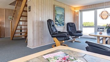 A room with a wooden interior, a black leather chair, a table with a magazine, and a painting on the wall.