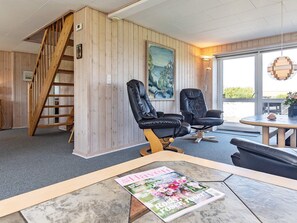 Une pièce au décor intérieur en bois, avec un fauteuil en cuir noir, une table sur laquelle repose un magazine et un tableau accroché au mur.