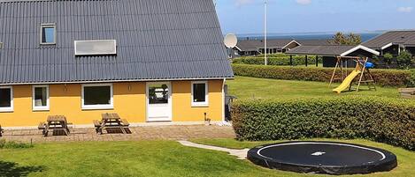 A residential building with a grey roof, a yellow facade, and a satellite dish. There is a playground with a slide and a swing set.