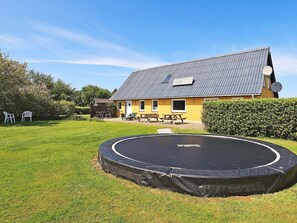 A residential property with a trampoline in the yard, a yellow house with a grey roof, and outdoor furniture. - Spacious Holiday Home in Vinderup near Fjord (Vinderup)