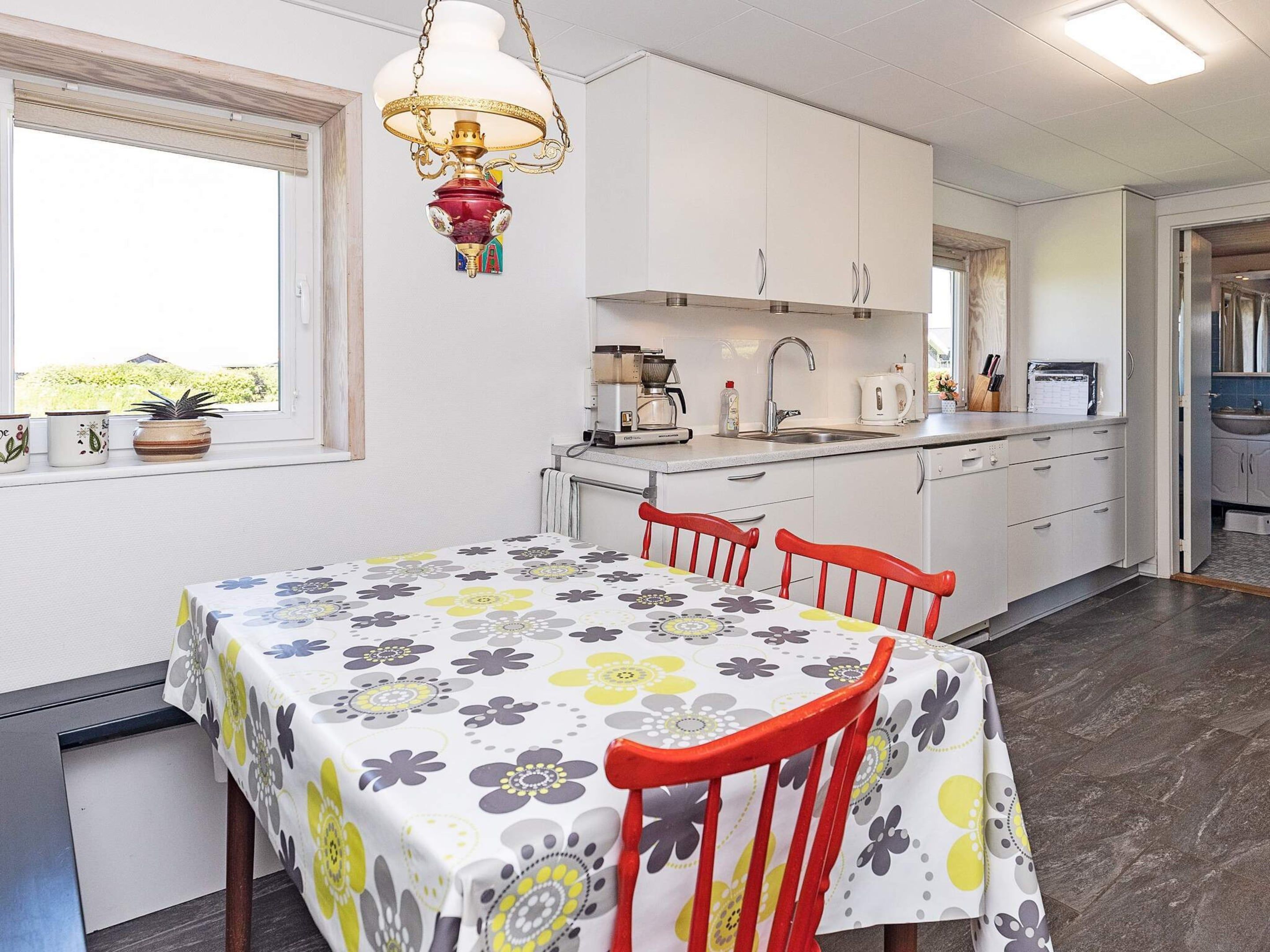 Una cocina moderna con armarios blancos, una mesa de comedor con mantel floral y una silla roja.