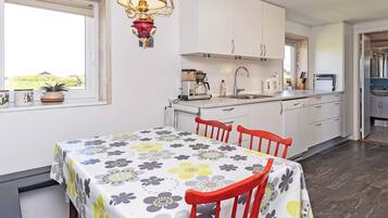 Una cocina moderna con armarios blancos, una mesa de comedor con mantel floral y una silla roja.
