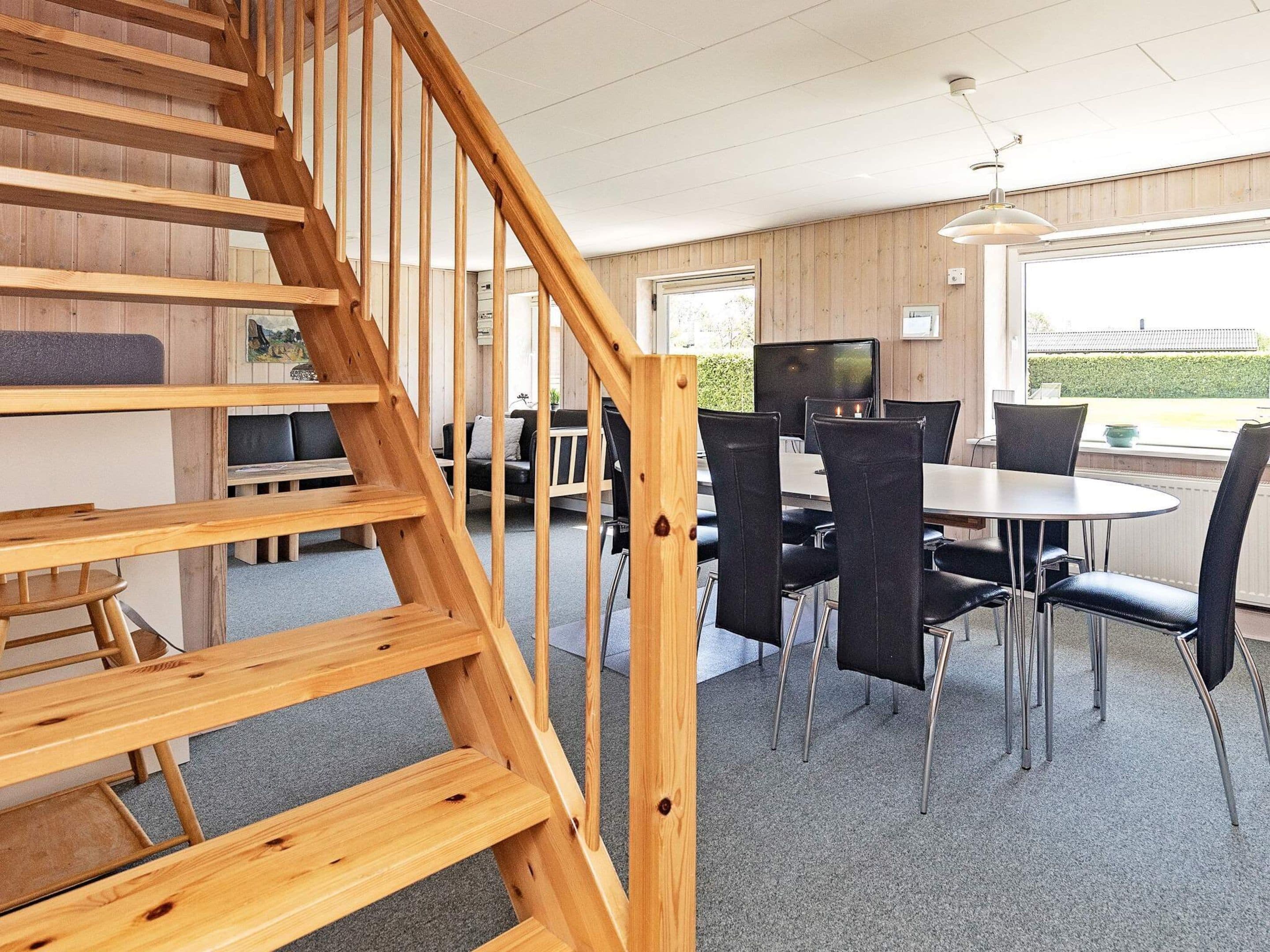 Una escalera de madera conduce a un comedor con una mesa y sillas.