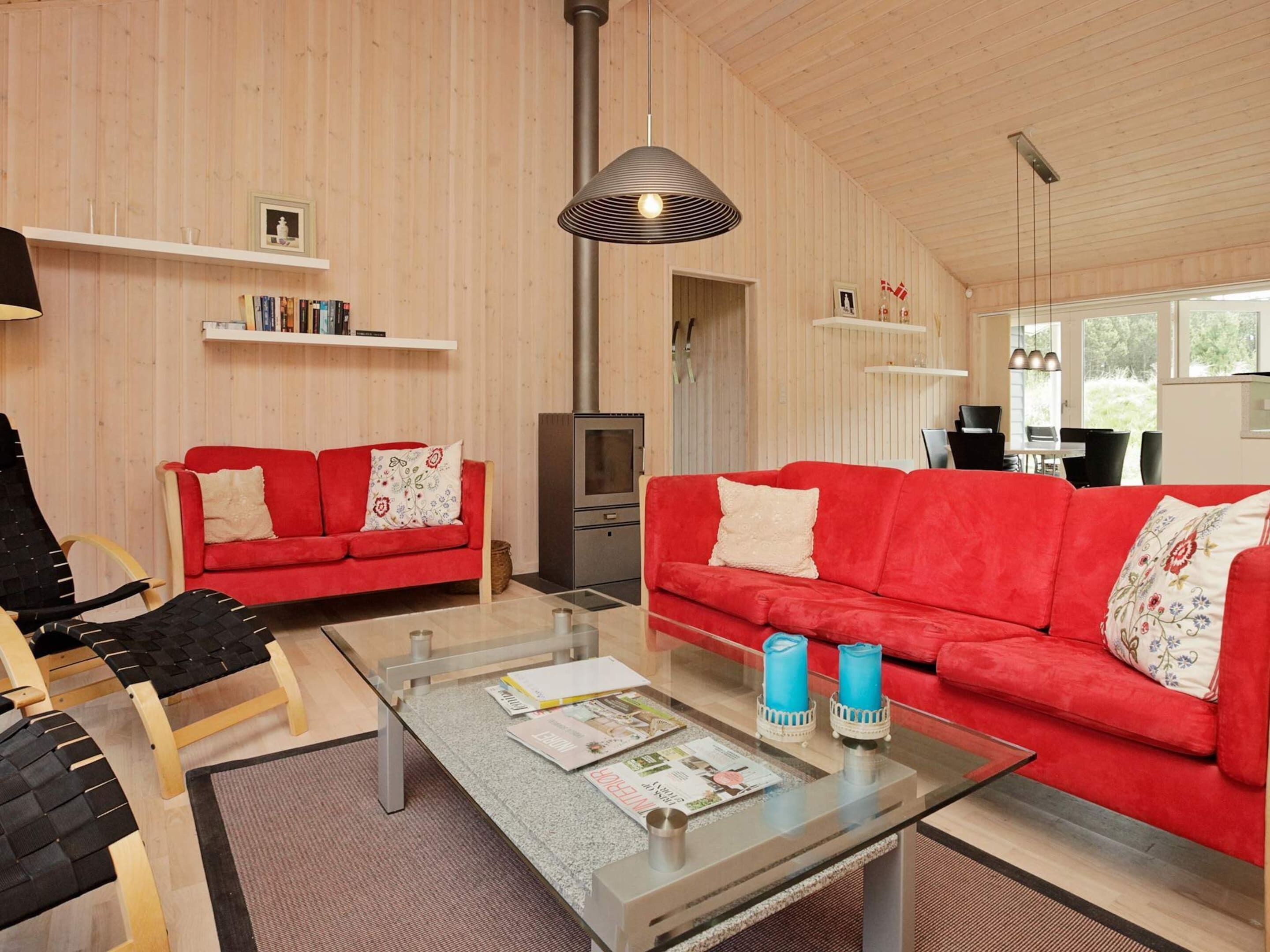 Un salon moderne avec deux canapés rouges, une table basse en verre sur laquelle sont posés des magazines, un fauteuil noir et une cheminée.
