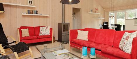 Un salon moderne avec deux canapés rouges, une table basse en verre sur laquelle sont posés des magazines, un fauteuil noir et une cheminée.