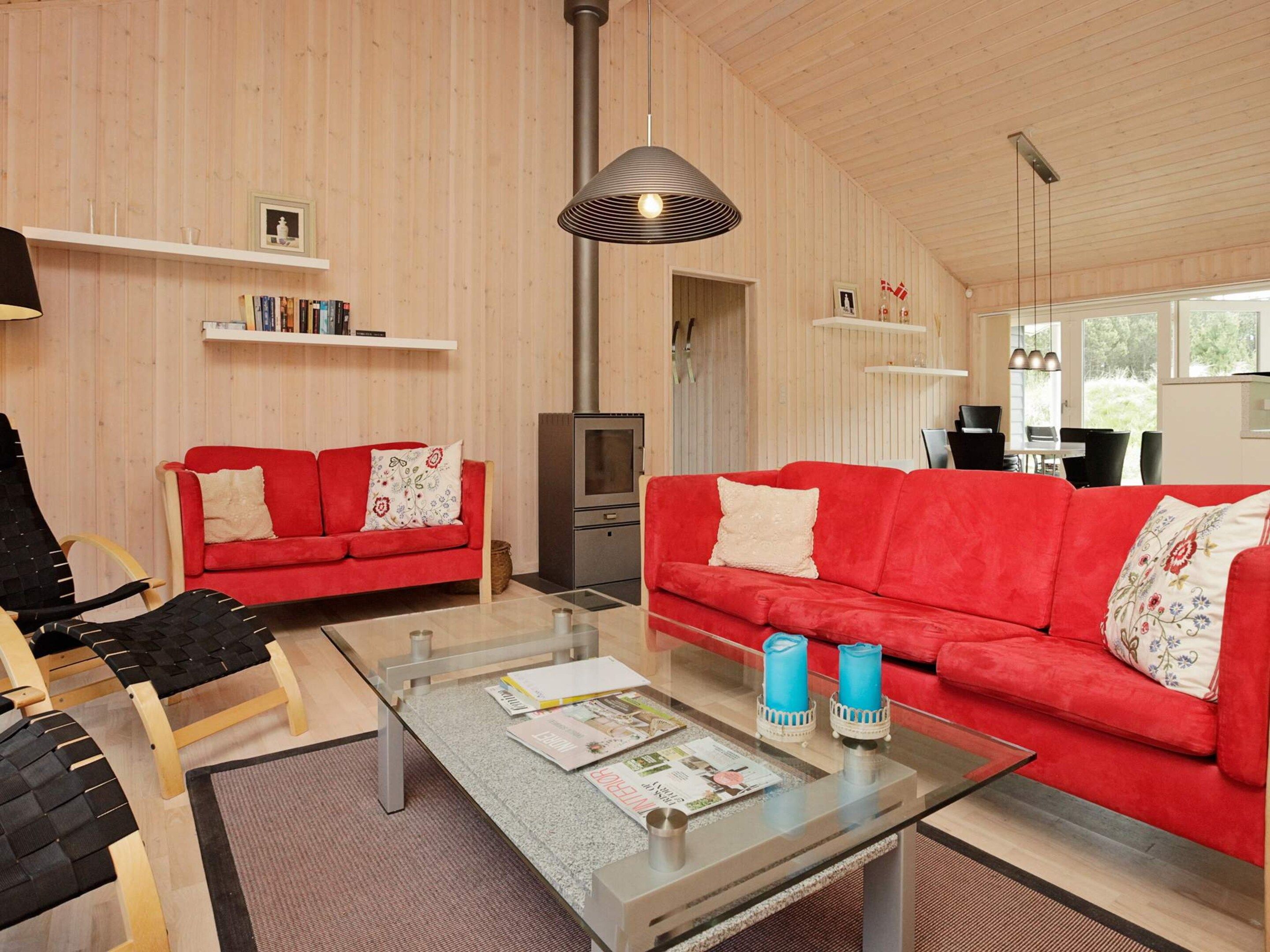Een moderne woonkamer met twee rode banken, een glazen salontafel met tijdschriften en een open haard.