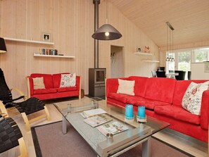 Un salon moderne avec deux canapés rouges, une table basse en verre sur laquelle sont posés des magazines et une cheminée.