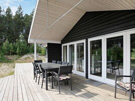 Una terraza con mesa y sillas, un espacio cubierto con techo inclinado y una puerta de cristal que da a un jardín.