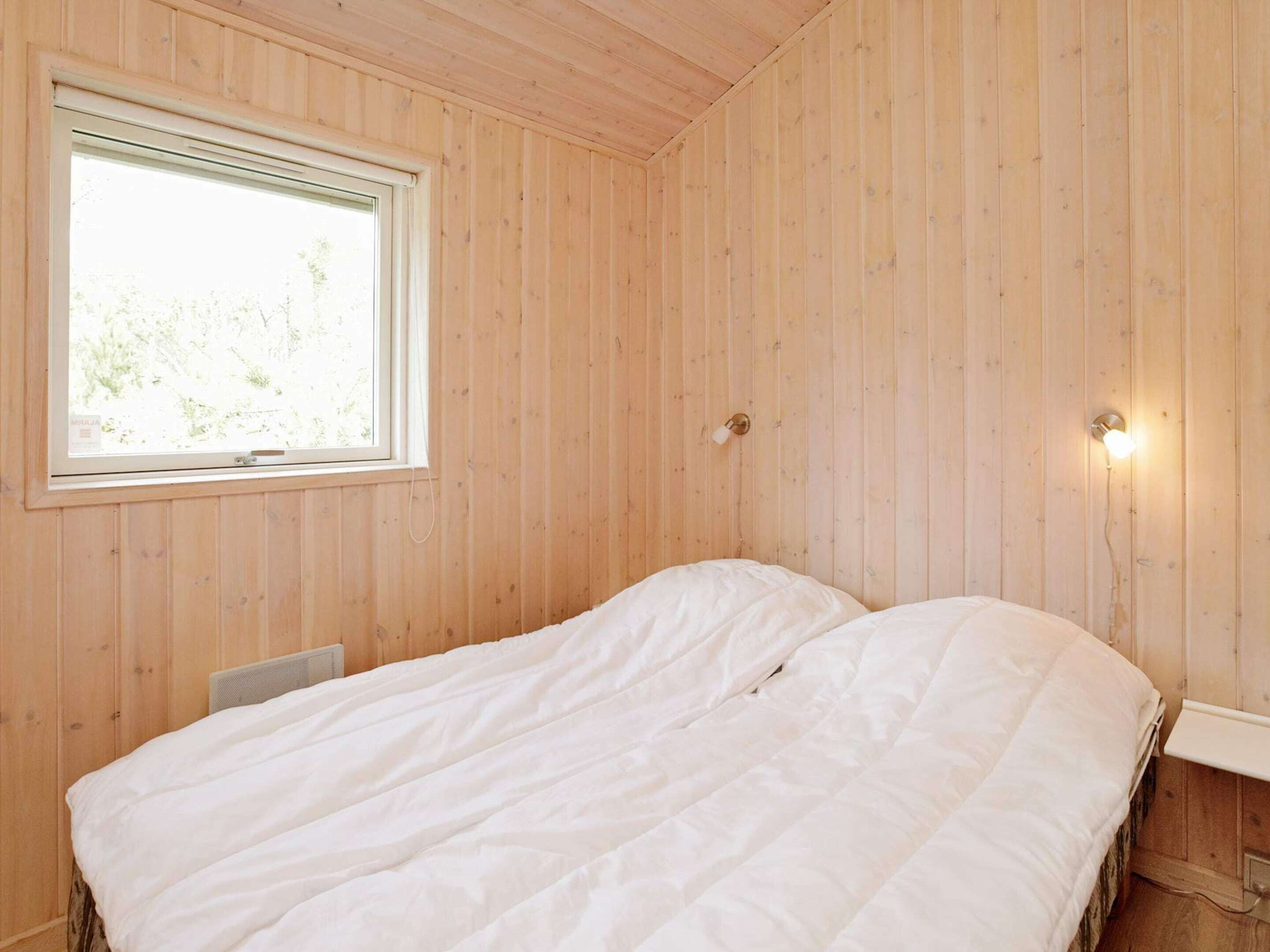 A room with wooden walls, a single bed with white bedding, a window, and a wall-mounted light fixture.