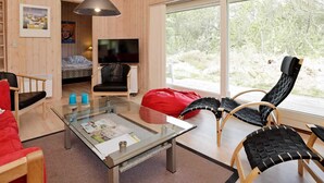 A modern living room with a glass coffee table, a red bean bag, and a TV in a wooden room with large windows. - 4 Star Holiday Home in Albaek (Aalbaek)