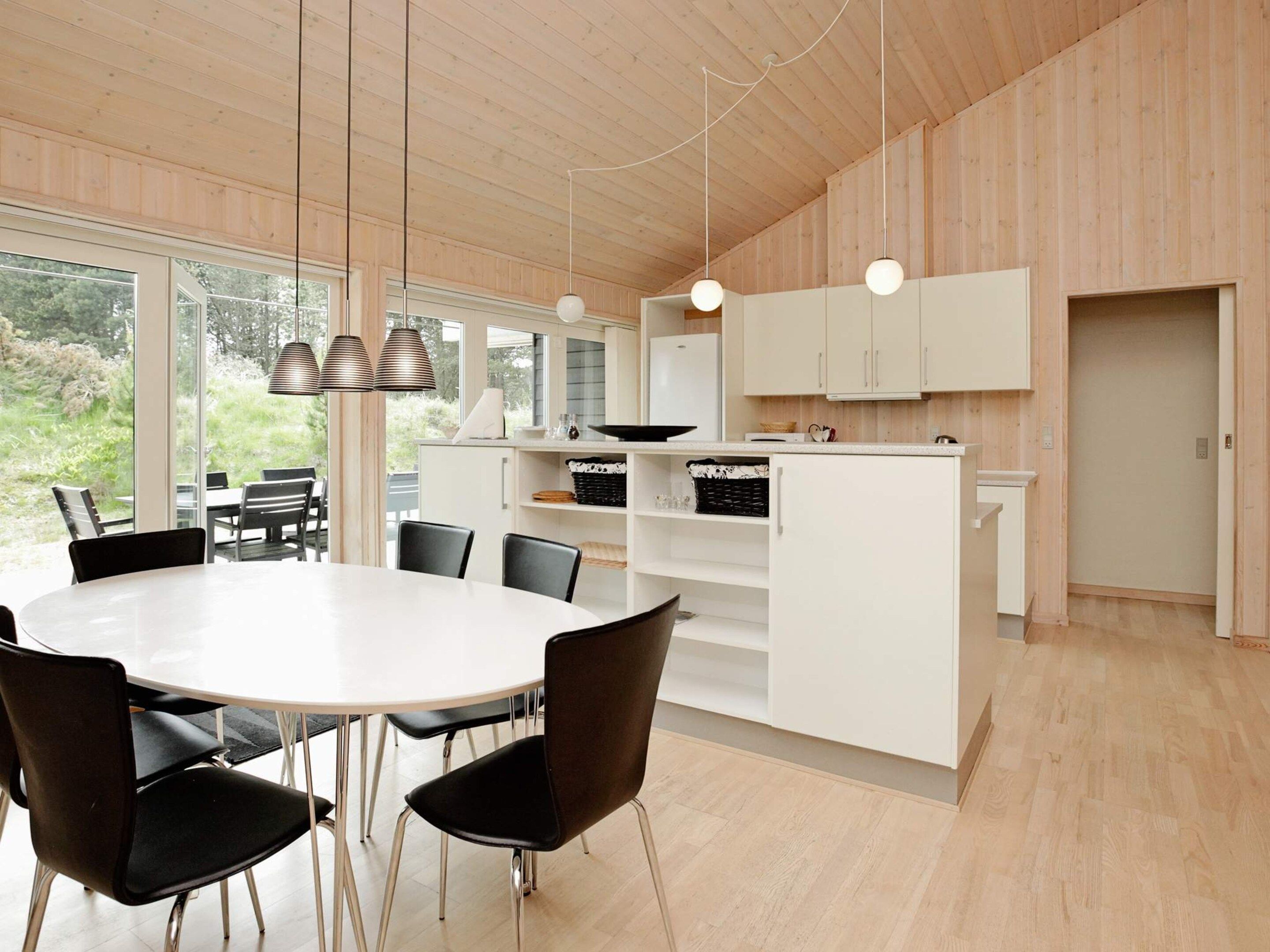 Een moderne keuken met witte kasten, een eethoek met een ronde tafel en stoelen, en uitzicht op groen buiten.